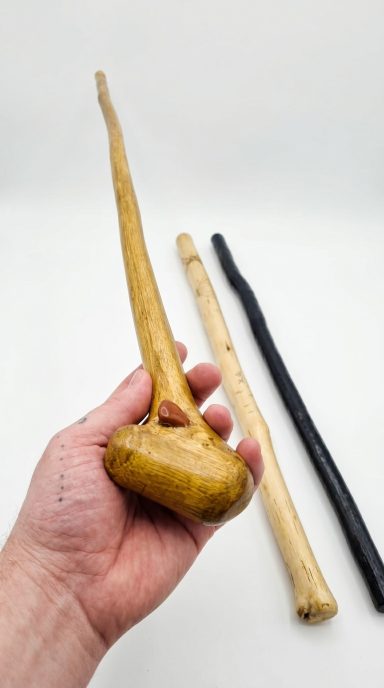 Full Length Wooden Walking Staff Full length handcrafted light brown walking staff held by hand with artisan staffs in the background
